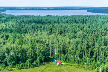 Fototapeta na wymiar Aerial view of mixed forest and distant river and small house at bottom of ski slope