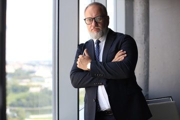 Fototapeta premium Thoughtful mature business man in full suit looking away while standing near the window.