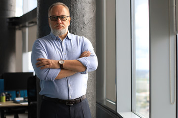 Thoughtful mature business man in a corporate suit looking away while standing near the window.