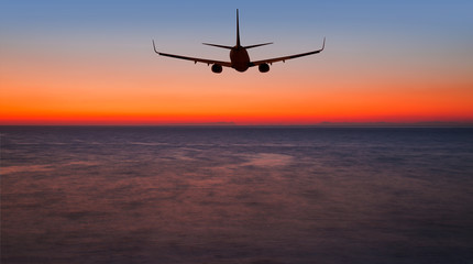 Airplane flying above tropical sea at sunset