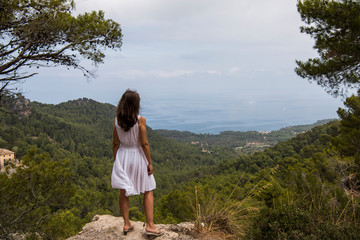 Naklejka premium Cap de Formentor, Mallorca, Spain. Young woman in front of beautiful scenery with the sea, rocks and cloudy sky.