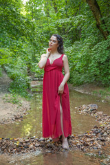 Beautiful girl in a chic red dress posing in the fairy forest.