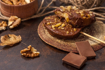 Slices of apples in chocolate, caramel glaze and walnuts on skewers on a dark background