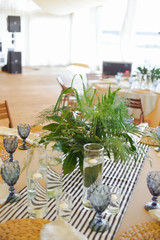 beautiful elegant wedding table decorated with glass candlesticks, glasses, plates, a bouquet of greens with a tablecloth