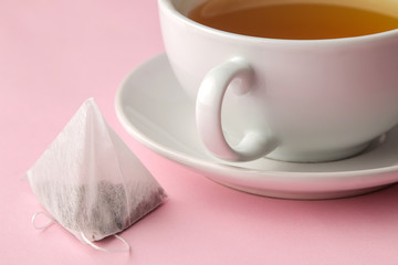 Tea bag pyramid and cup with tea on a delicate pink background. to make tea.