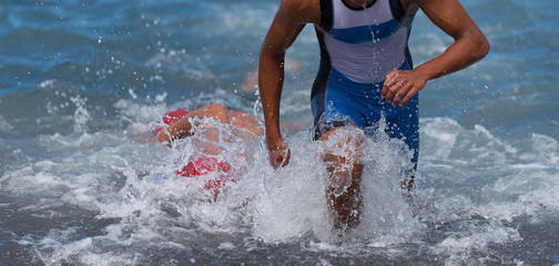 Triathlete swimmer running out of ocean finishing swim race.Fit man ending swimming sprinting...