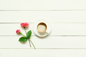 A cup of fresh hot cappuccino with two pink roses on a white wooden table. Top view with copy space, flat lay.