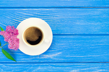 A cup of fresh hot coffee with pink flowers on a blue wooden table. Top view with copy space, flat lay.