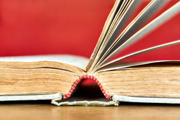 Closeup of weathered old book. Open antique book with red and white decorative headband and footband and pages against a red background. Side view with shallow depth of field and copy space.    