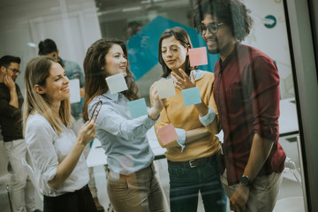 Young business people discussing in front of glass wall using post it notes and stickers