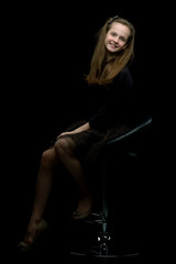 Fototapeta na wymiar Charming girl teenager sitting on a chair in the studio on a bla