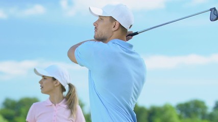 Woman golf beginner player admiring man professionally hitting ball, half-swing