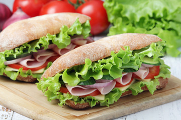 Two sandwiches with fresh vegetables, ham and cheese in ciabatta bread