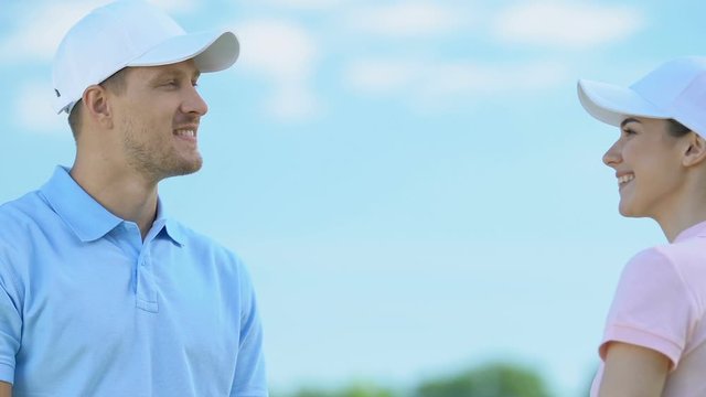 Smiling man and woman in golf uniform giving high five, flirt after training