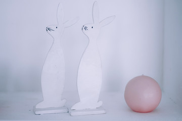 Two white hares carved from a tree with a pink ball stand on a white concrete background