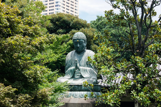 Japanese sitting Buddha statue between trees in a park near the city