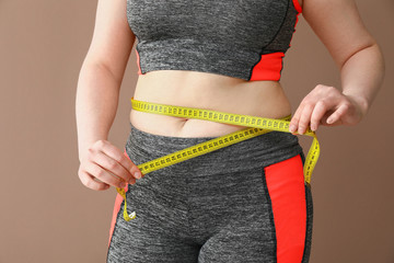 Overweight woman with measuring tape on color background. Weight loss concept