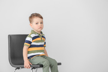 Little boy with autistic disorder sitting on chair against light background