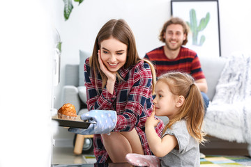 Young woman and her little daughter baking tasty muffins at home
