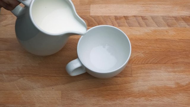 Close up of pouring milk in white cupon a wooden background.