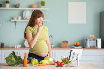 Beautiful pregnant woman with healthy vegetables in kitchen