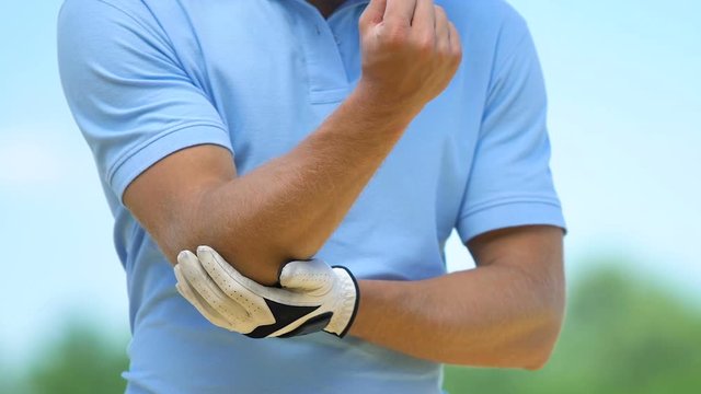 Man golf player warming up and massaging muscles of elbow, cramp, trauma
