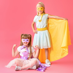 Cute little girls dressed as superheroes on color background
