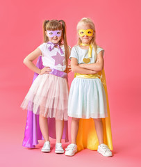 Cute little girls dressed as superheroes on color background
