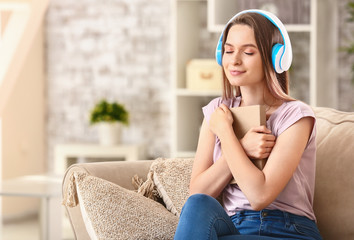 Beautiful young woman listening to audiobook while sitting on sofa at home