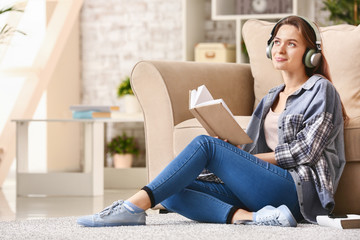 Beautiful young woman listening to music while reading book at home