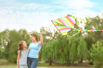 Young woman with little daughter flying kite outdoors