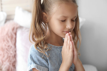 Cute little girl praying in bedroom