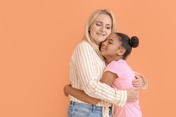 Happy woman hugging her African-American daughter on color background