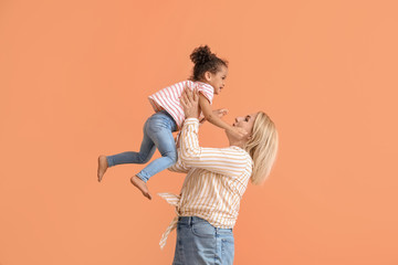 Happy woman and her little African-American daughter on color background
