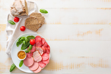 Plate with assortment of sausages, sauce and bread on light table