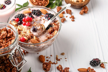 Granola crispy honey muesli with natural yogurt, fresh berries, chocolate and nuts in a glass bowl against a light background, healthy food, horizontal orientation, copy space