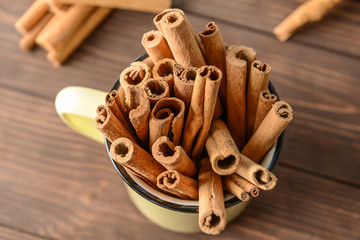 Mug with aromatic cinnamon sticks on wooden table