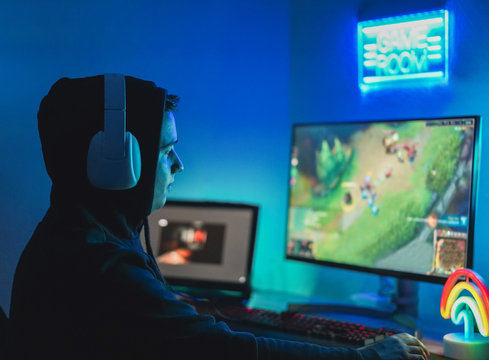 Young streamer gamer playing at strategy game in broadcast browser - Male guy having fun gaming and streaming online - New technology game trends and entertainment concept - Focus on his face