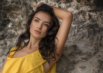 Naklejka premium Woman in long yellow dress on rocky beach on Bali, Indonesia. Summer time. Dark hair brunette