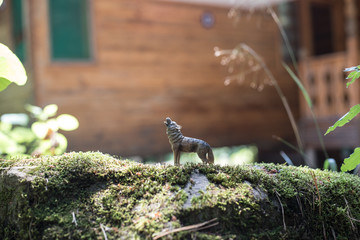 Howling wolf in the forest. Mini wolf figure standing on the forest ground.