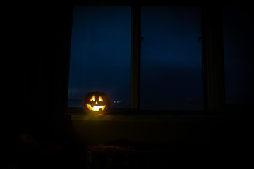 Scary Halloween pumpkin in the mystical house window at night or halloween pumpkin in night on room with blue window. Symbol of halloween in window.