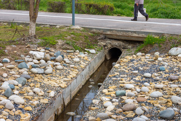 The storm sewer ditch with the concrete tube under pedestrian walkway and with boulders on the sides