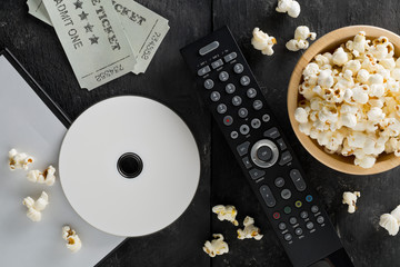 DVD or blu ray movie disc with tv remote control, movie tickets and bowl of popcorn on dark...