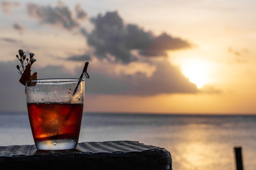 An iced summer cocktail isolated in front of a sunset over the sea