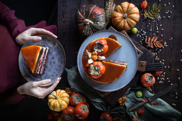 Autumn cake with persimmon and caramel with a pumpkin and a girl in a burgundy dress on a black background, Atmospheric dark food photos, Pastry Homemade in Womans hands, Selective focus