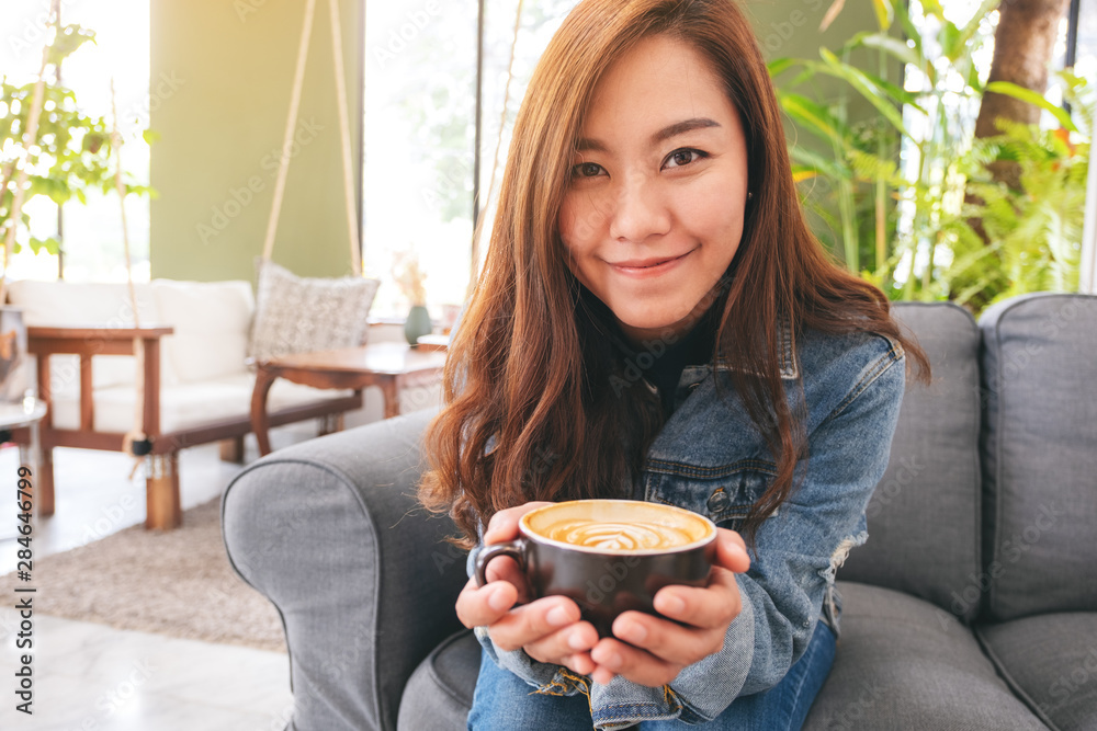 Poster Closeup image of a beautiful asian woman holding a cup of hot coffee in cafe