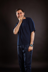 A young handsome man laughs contagiously, covering his mouth with his hand. Black background. Vertical.