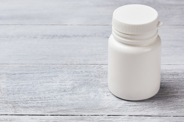 Plastic white jar for pills on gray wood background copyspace