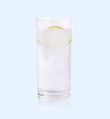 Green lime sliced falling in the soda water of glass on the soft blue background