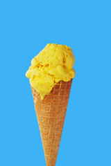 Yellow mango ice cream in a waffle cone on a light blue background. Close-up